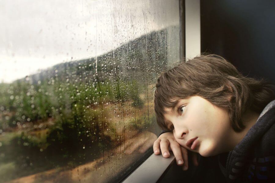 Ein Kind legt den Kopf auf die Fensterbank Draußen regnet es