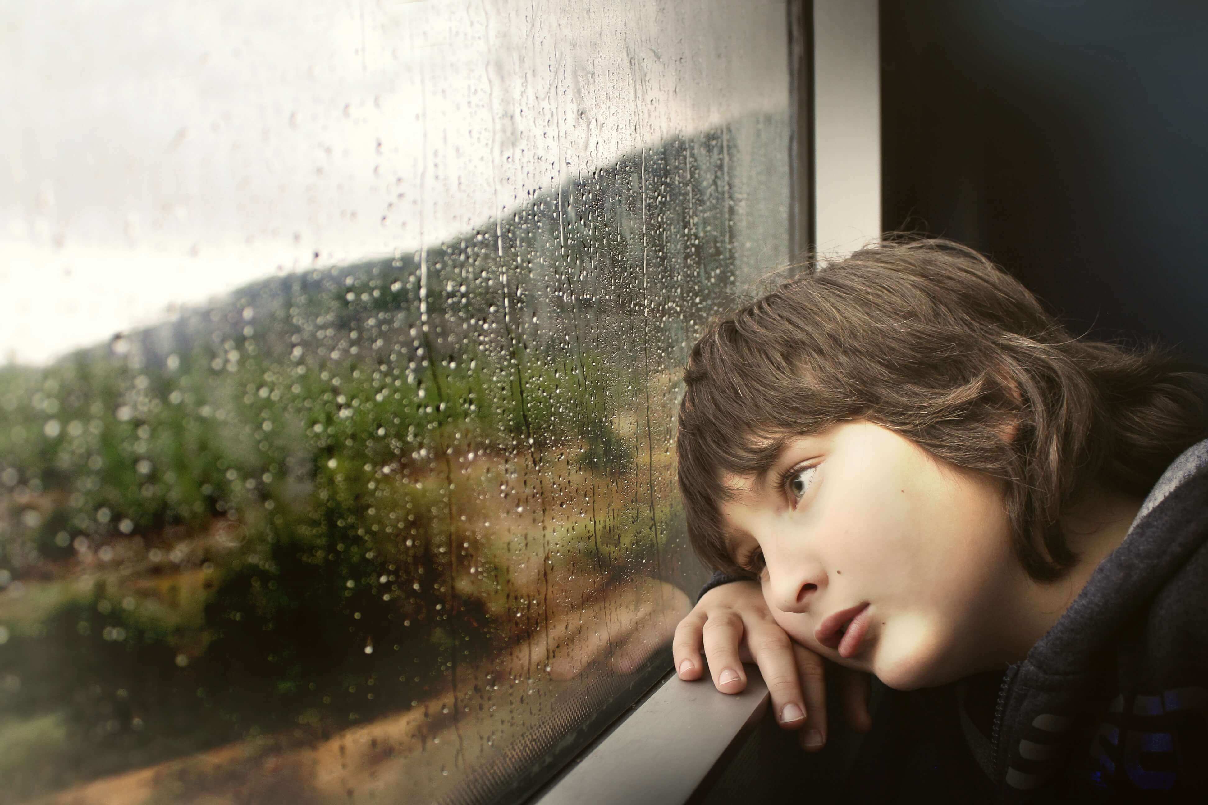 Ein Kind legt den Kopf auf die Fensterbank Draußen regnet es
