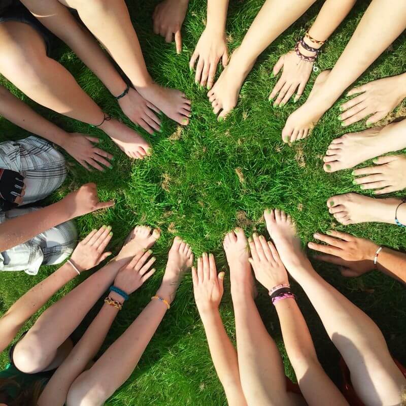 Eine Gruppe von Kindern sitzen auf einer Wiese. Sie formen einen Kreis mit ihren Händen und Füßen