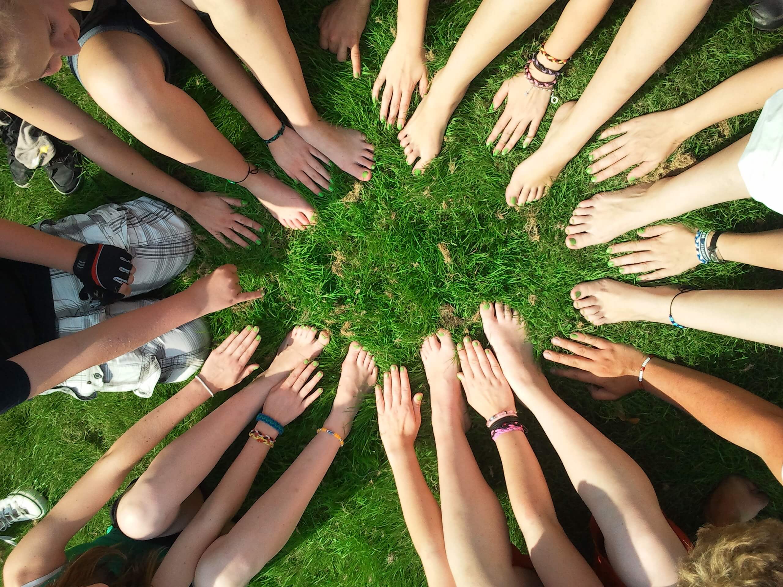 Eine Gruppe von Kindern sitzen auf einer Wiese. Sie formen einen Kreis mit ihren Händen und Füßen