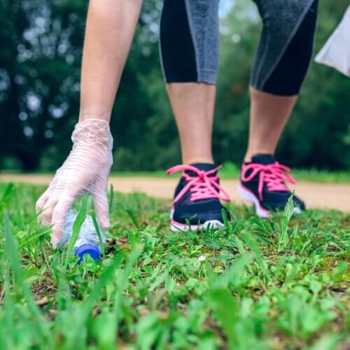 Eine Frau mit Einweghandschuhen hebt eine Plastikflasche vom Gras auf
